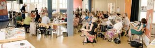 Viele Menschen in einem Raum auf der DEAB-Mitgliederversammlung, vorne der Vorstand und ein Referent, gegenüber die Mitglieder und Mitarbeiter*innen