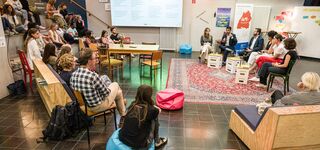 Publikum schaut auf ein Podium und hört einer Diskussion mit 6 Personen zu